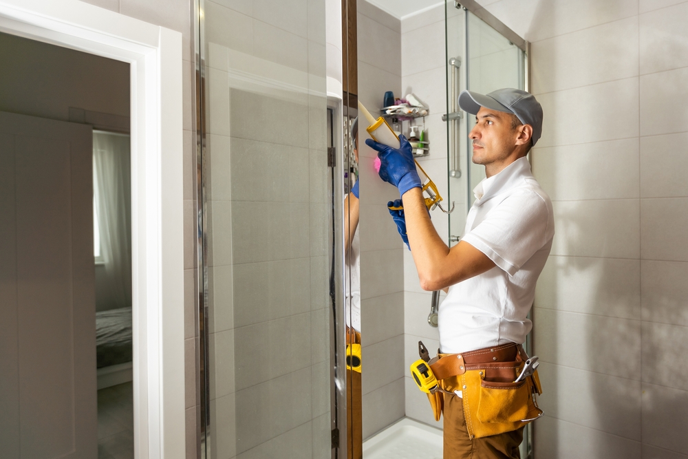 Technician repairing a frameless shower glass door in a modern residential bathroom